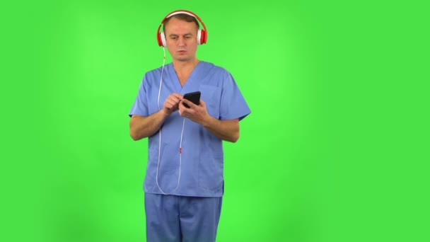 Büyük kırmızı kulaklıklı bir doktor cep telefonunda müzik açar. Yeşil Ekran — Stok video