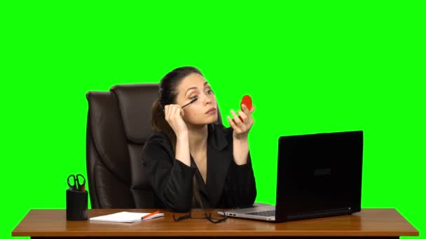 Frau sitzt im Ledersessel am Schreibtisch und trägt Wimpern mit Wimperntusche auf, schaut in einen roten Spiegel auf grünem Bildschirm — Stockvideo