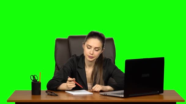 Гарненька жінка сидить на робочому місці з блокнотом і олівцем, думає важко, дратує зітхання і котиться очима. Зелений екран — стокове відео