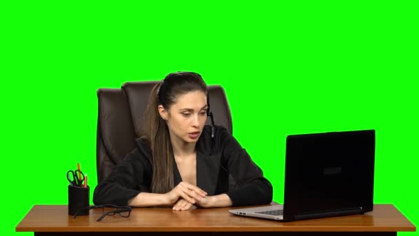 Zakelijke vrouw in hoofdtelefoon spreekt door webcam en kijk naar laptop. Groen scherm — Stockvideo