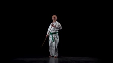 Beyaz kimonolu Kendo dövüşçüsü siyah arka planda bambu bokken ile dövüş sanatları yapıyor. Yavaş çekim