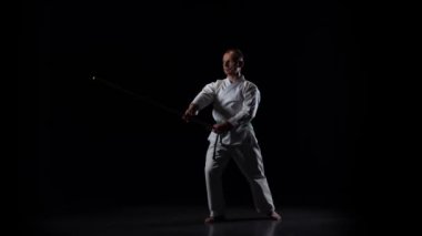 Beyaz kimonolu Kendo dövüşçüsü siyah arka planda bambu bokken ile dövüş sanatları yapıyor. Yavaş çekim