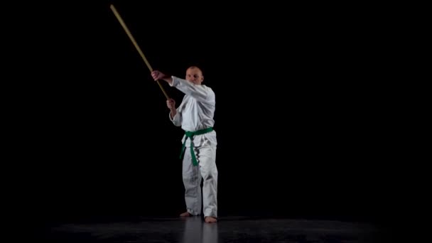 Kendo fighter na białym kimono ćwiczy sztukę walki z bambusowym bokken na czarnym tle. Zwolniony ruch — Wideo stockowe