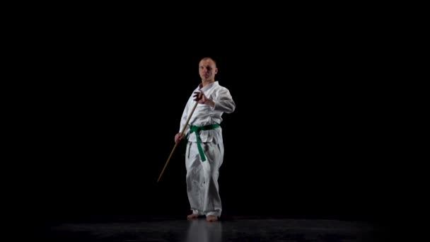 Kendo fighter na białym kimono ćwiczy sztukę walki z bambusowym bokken na czarnym tle. Zwolniony ruch — Wideo stockowe