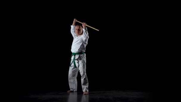 Боец Кендо на белом кимоно практикует боевое искусство с бамбуковым боккеном на черном фоне. Медленное движение — стоковое видео