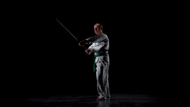 Борці кендо на білому кімоно практикують бойове мистецтво з бамбуковим боккеном на чорному тлі. Повільний рух — стокове відео