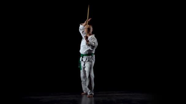 Kendo fighter on white kimono practicing martial art with the bamboo bokken on black background. Slow motion — Stock Video