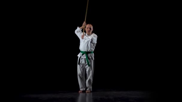 Kendo fighter on white kimono practicing martial art with the bamboo bokken on black background. Slow motion — Stock Video