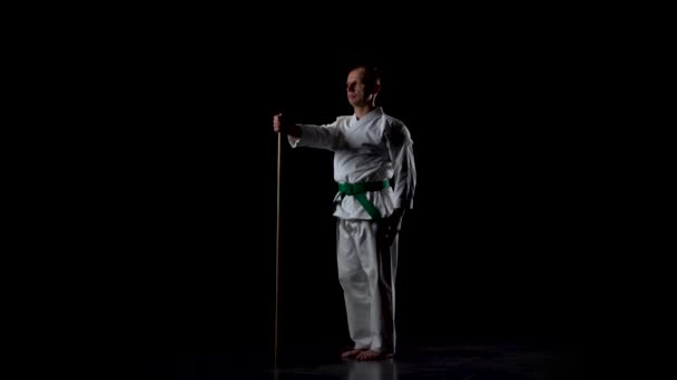 Kendo fighter på vit kimono tränar kampsport med bambu bokken på svart bakgrund. Långsamma rörelser — Stockvideo