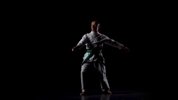 Kendo fighter on white kimono practicing martial art with the bamboo bokken on black background. Slow motion — Stock Video