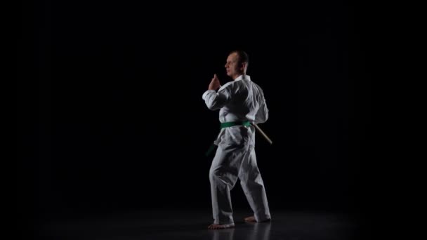 Kendo fighter på vit kimono tränar kampsport med bambu bokken på svart bakgrund. Långsamma rörelser — Stockvideo