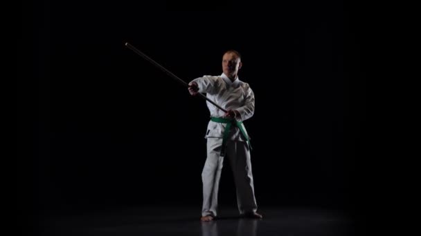 Kendo fighter på vit kimono tränar kampsport med bambu bokken på svart bakgrund. Långsamma rörelser — Stockvideo