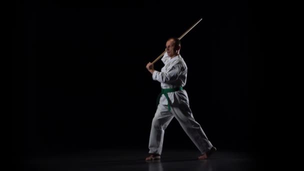 Kendo fighter på vit kimono tränar kampsport med bambu bokken på svart bakgrund. Långsamma rörelser — Stockvideo