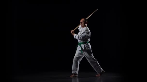 Kendo-Kämpfer auf weißem Kimono, der Kampfkunst mit dem Bambusbokken auf schwarzem Hintergrund praktiziert. Zeitlupe — Stockvideo