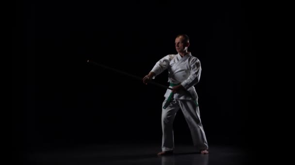 Kendo lutador no quimono branco praticando arte marcial com o bokken de bambu no fundo preto. Movimento lento — Vídeo de Stock