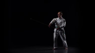 Beyaz kimonolu Kendo dövüşçüsü siyah arka planda bambu bokken ile dövüş sanatları yapıyor. Yavaş çekim