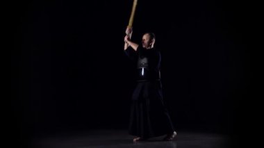 Siyah arka planda bambu bokken ile dövüş sanatları yapan erkeksi Kendo savaşçısı. Yavaş çekim