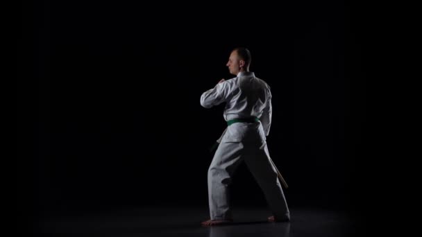 Kendo fighter på vit kimono tränar kampsport med bambu bokken på svart bakgrund. Långsamma rörelser — Stockvideo