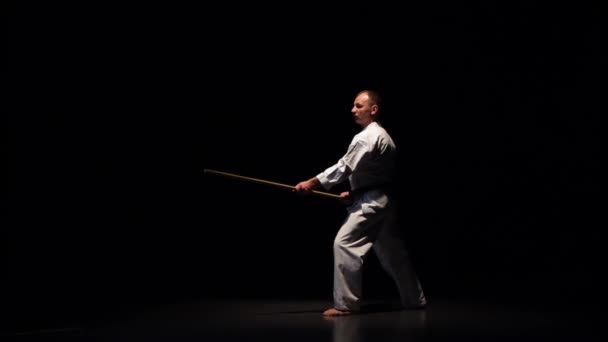 Kendo fighter on white kimono practicing martial art with the bamboo bokken on black background. Slow motion — Stock Video