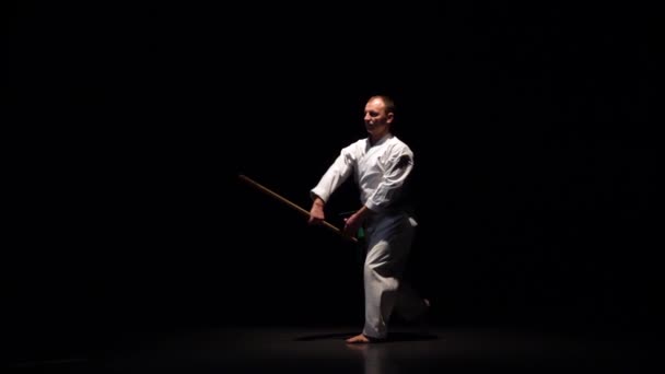 Kendo bojovník na bílém kimonu cvičí bojové umění s bambusovým bokken na černém pozadí. Zpomalený pohyb — Stock video