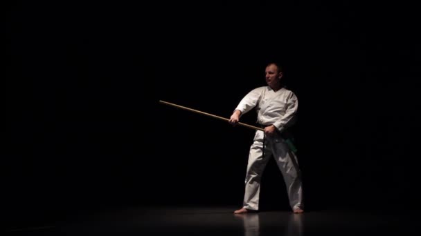 Kendo fighter on white kimono practicing martial art with the bamboo bokken on black background. Slow motion — 비디오
