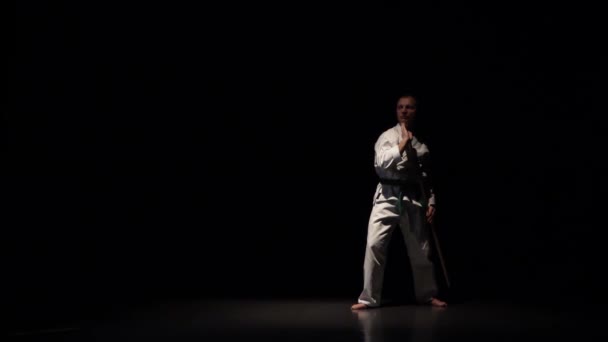 Luchador Kendo en kimono blanco practicando arte marcial con el bokken de bambú sobre fondo negro. Movimiento lento — Vídeo de stock