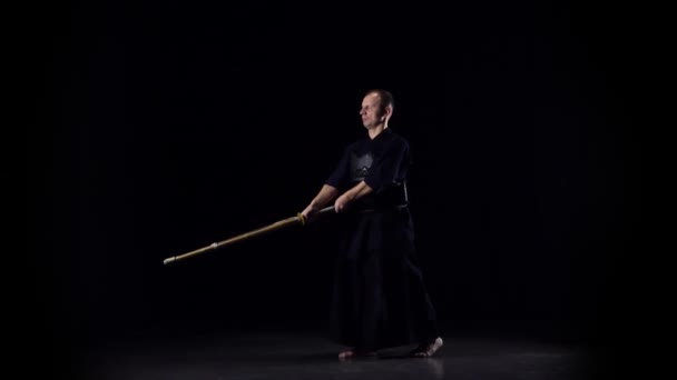 Masculine Kendo πολεμιστής εξάσκηση πολεμικές τέχνες με το μπαμπού bokken σε μαύρο φόντο. Αργή κίνηση — Αρχείο Βίντεο
