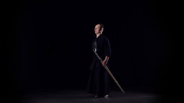 Férfias Kendo harcos harcművészetet gyakorol a bambusz bokkennel a fekete háttéren. Lassú mozgás. — Stock videók