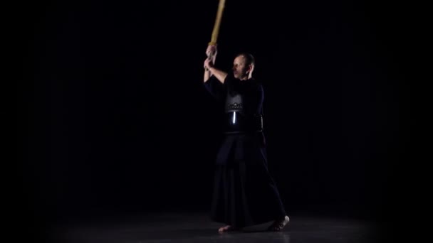Masculine Kendo πολεμιστής εξάσκηση πολεμικές τέχνες με το μπαμπού bokken σε μαύρο φόντο. Αργή κίνηση — Αρχείο Βίντεο