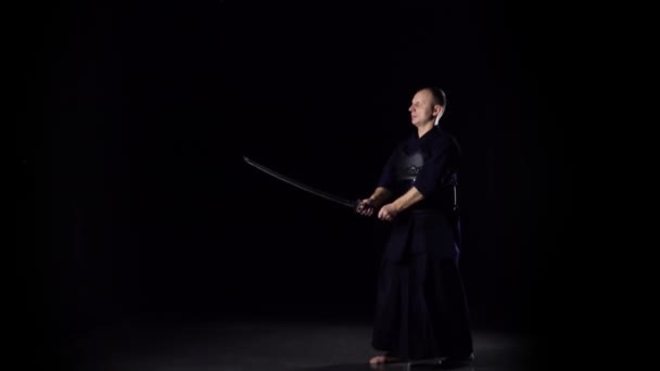 Kendo-Krieger, der Kampfkunst mit dem Katana-Schwert auf schwarzem Hintergrund praktiziert. Zeitlupe — Stockvideo