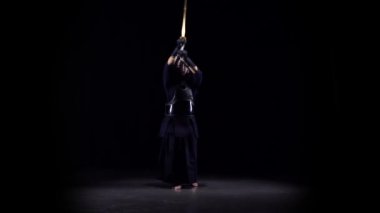 Siyah arka planda bambu bokken ile dövüş sanatları yapan erkeksi Kendo savaşçısı. Yavaş çekim