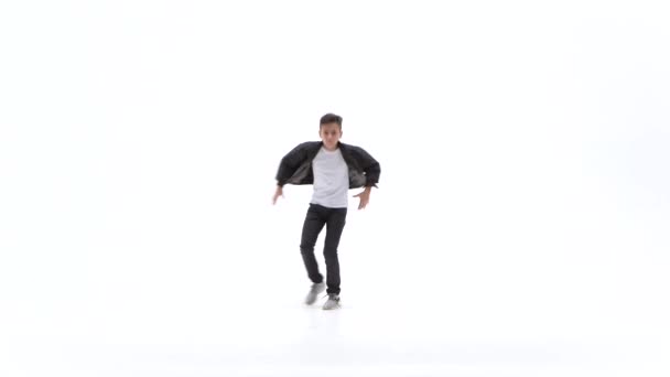Маленький хлопчик танцює сучасний танець на білому тлі в чорних шкіряних куртках і джинсах — стокове відео