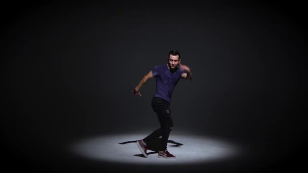 Mann tanzt Breakdance auf dunklem Hintergrund in schlichtem grauem T-Shirt und grauer Jeans — Stockvideo