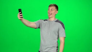 Komik adam stüdyoda yeşil ekranda akıllı telefonuyla selfie çekiyor..