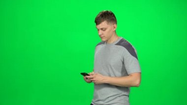 Gülümseyen adam stüdyodaki yeşil ekranda akıllı telefonuyla mesajlaşıyor..