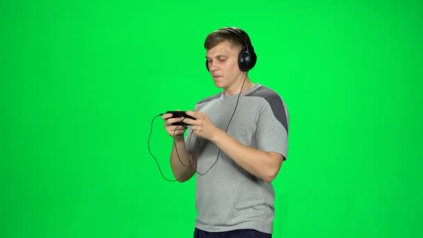 Guy in big black headphones goes and texting with smartphone on green screen at studio. — Stock Video