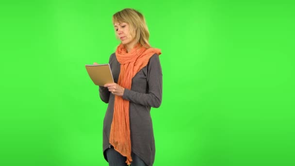 Middle aged blonde woman is thinking, then writing with pencil in notebook. Green screen — Stock Video