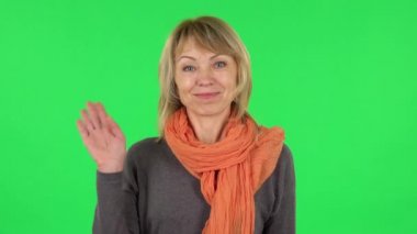 Orta yaşlı sarışın kadın portresi el sallıyor ve el sallıyor. Buraya gel. Yeşil Ekran