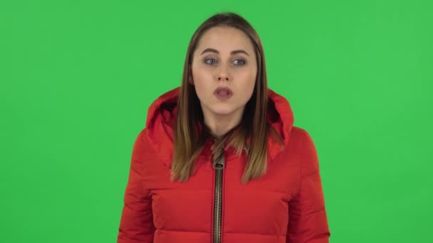 Das Porträt eines hübschen Mädchens in roter Daunenjacke ist aufgebracht, fuchtelt empört mit den Händen und zuckt mit den Schultern. Green Screen — Stockvideo