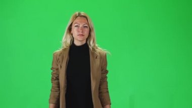 Blonde girl in a black turtleneck and stylish brown jacket going against a green screen. Slow motion