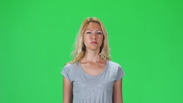 Ragazza bionda con una t-shirt grigia che va a guardare dritto nella fotocamera contro uno schermo verde. Rallentatore — Video Stock