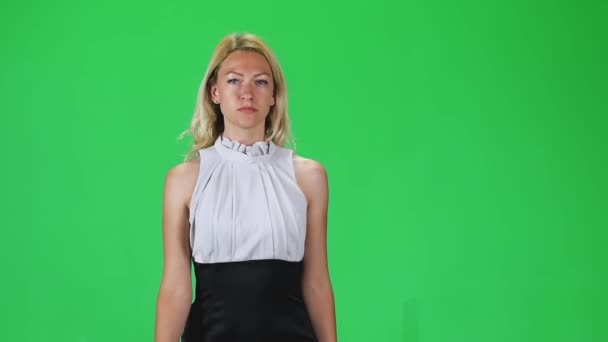 Blonde girl in black and white dress going and looking straight into the camera against a green screen. Slow motion — ストック動画