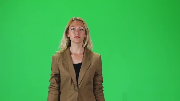 Menina loira em uma jaqueta marrom elegante indo e olhando diretamente para a câmera contra uma tela verde. Movimento lento — Vídeo de Stock