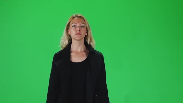 Блондинка в черном пальто смотрит прямо в камеру на зеленый экран. Медленное движение — стоковое видео