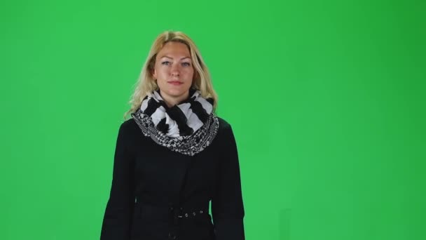 Blonde girl in a black and white scarf and coat going against a green screen. Slow motion — Stockvideo