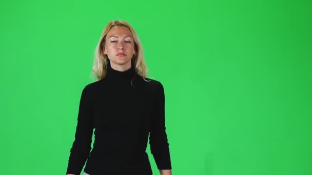 Blonde girl in black turtleneck and grey skirt going against green screen. Slow motion — Stock video