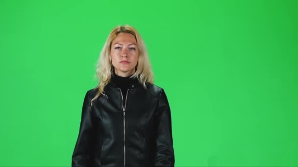 Fille blonde en veste en cuir noir va et regarde directement dans la caméra contre un écran vert. Mouvement lent — Video