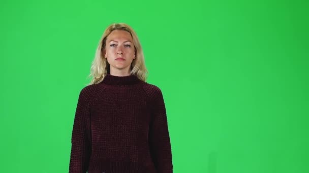 Blonde girl in pomegranate sweater going and looking straight into the camera against a green screen. Slow motion — Stock video