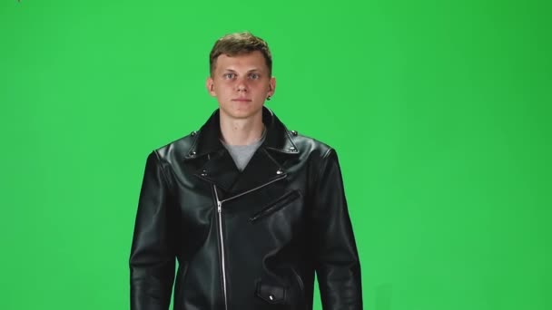 Giovane uomo in giacca di pelle nera in corso e guardando avanti su uno sfondo verde. Rallentatore . — Video Stock