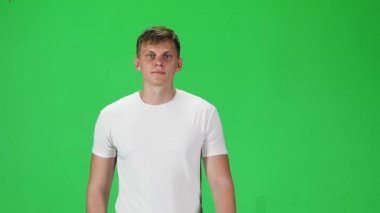 Young man in a white t-shirt going and looking forward against a green background. Slow motion.